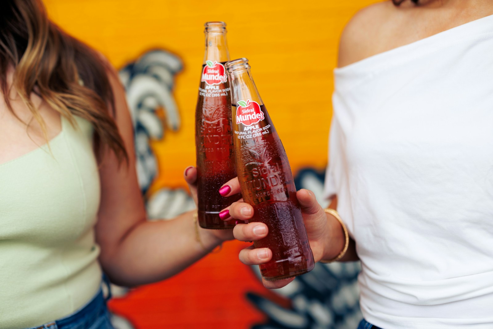 Two women standing next to each other holding bottles of soda